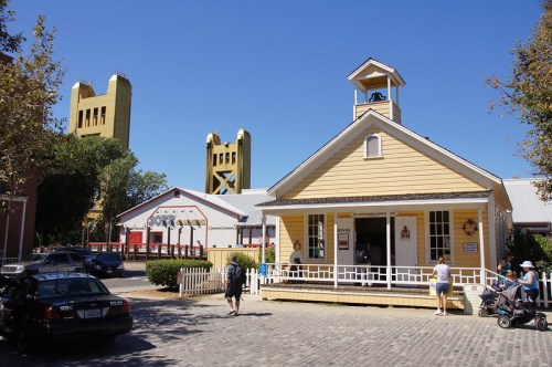 Historic yellow building with a bell tower, surrounded by trees and people, with the iconic towers in the background.