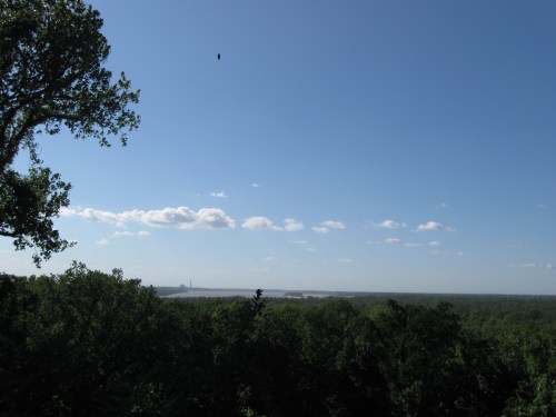 A clear blue sky with scattered clouds above a lush green landscape and distant horizon.