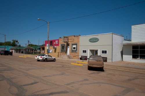 A quiet street scene featuring several buildings and parked cars under a clear blue sky.