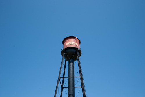 A tall water tower with a red tank labeled "REGENT" against a clear blue sky.