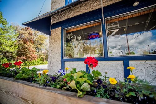 A close-up of a flower planter in front of a shop with an "Open" sign in the window. Bright flowers add color.