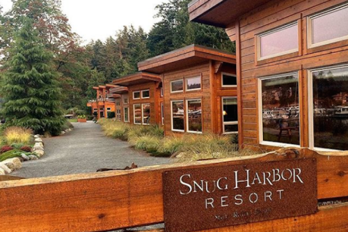 Wooden cabins line a pathway at Snug Harbor Resort, surrounded by trees and greenery.