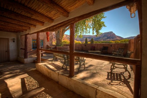 A rustic patio with wooden beams, overlooking a scenic mountain view and shaded by trees.