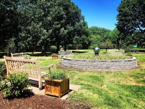 A serene garden with benches surrounding a circular flower bed and a decorative globe under a clear blue sky.