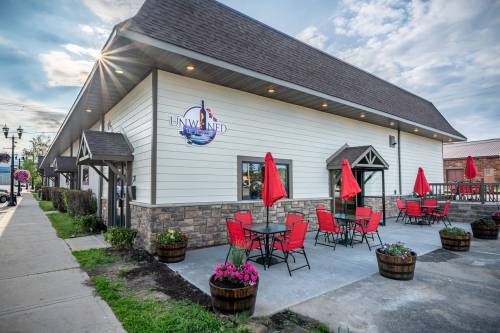 Exterior of a building named "Unwined," featuring red umbrellas and seating on a patio with flower planters.
