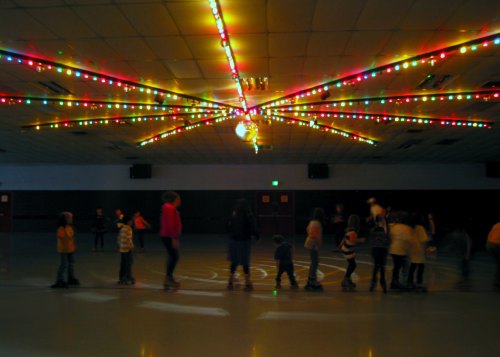 A group of children skating in a rink under colorful lights and a disco ball, creating a festive atmosphere.