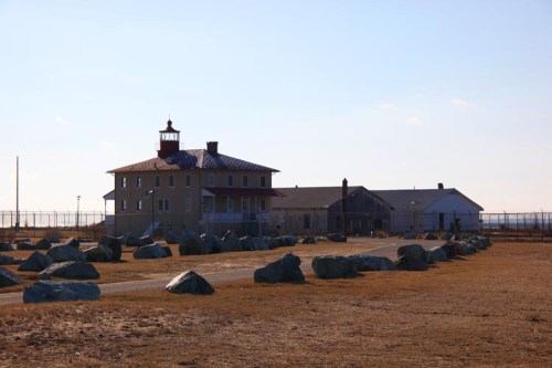 Historic building with a lighthouse-style tower, surrounded by large rocks and a fenced area under a clear sky.