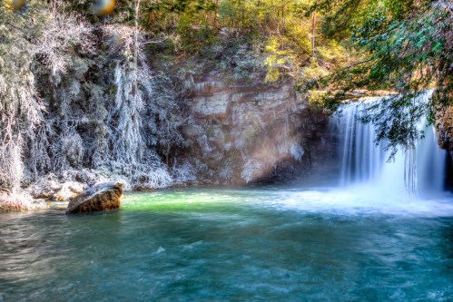 A serene waterfall cascades into a tranquil pool, surrounded by lush greenery and rocky cliffs.