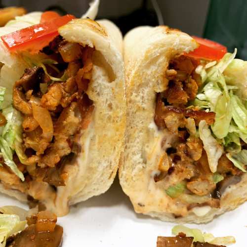 Close-up of a sandwich cut in half, filled with shredded meat, lettuce, tomatoes, and creamy sauce in a soft roll.