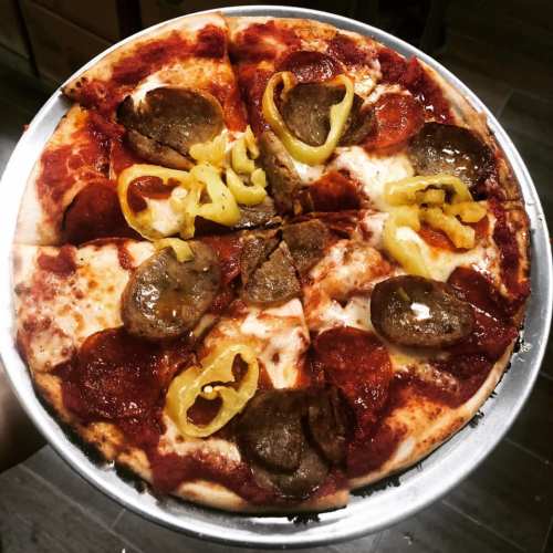 A freshly baked pizza topped with pepperoni, sausage, and yellow peppers, served on a round metal tray.