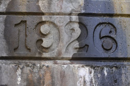 Close-up of a weathered stone wall featuring the year "1926" carved into it.