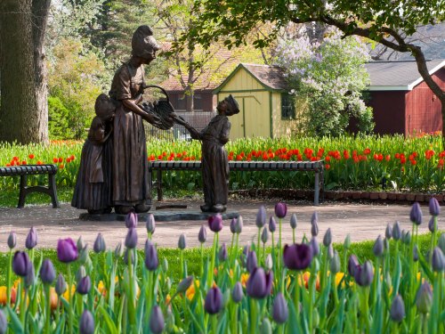 A bronze statue of a woman and two children in a garden filled with colorful tulips and a quaint background.
