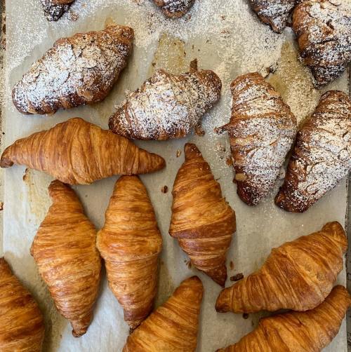 A variety of freshly baked croissants, some dusted with powdered sugar, arranged on parchment paper.