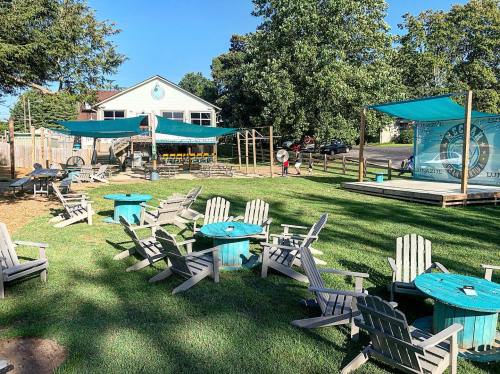 Outdoor seating area with turquoise tables and chairs, shaded by canopies, near a building and trees.