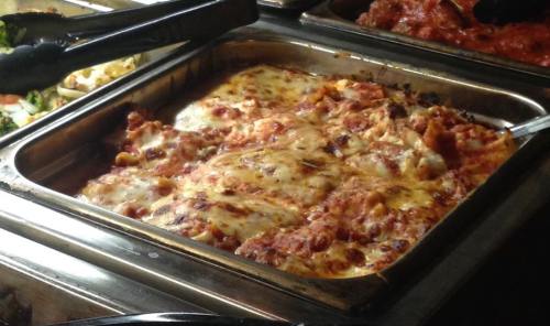 A tray of cheesy lasagna with layers of pasta, meat, and marinara sauce, served in a buffet setting.