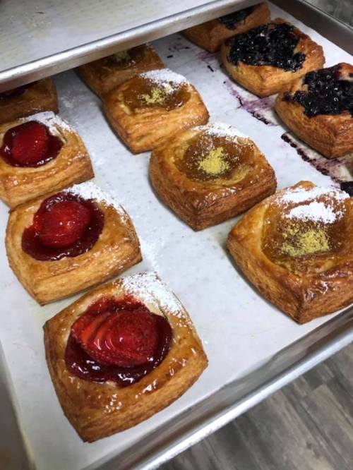 A tray of assorted pastries with fruit toppings, including strawberries and blueberries, dusted with powdered sugar.