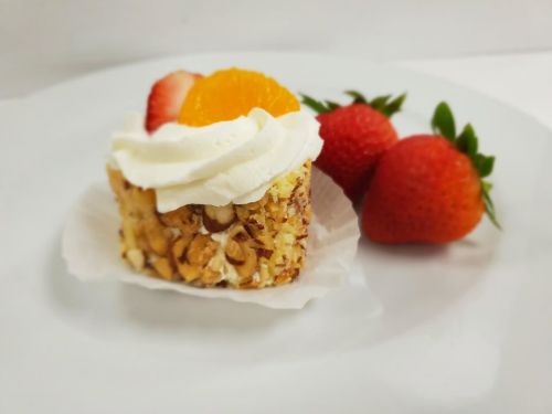 A small cake topped with whipped cream, orange slice, and strawberry, served on a white plate with fresh strawberries.