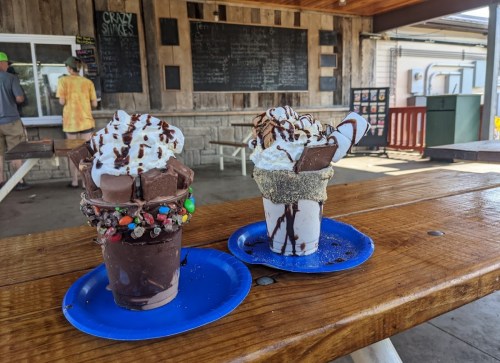 Two colorful ice cream sundaes topped with whipped cream, chocolate drizzle, and various toppings on blue plates.