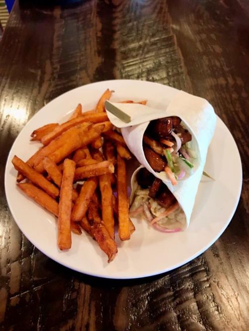 A plate with a wrap filled with grilled chicken and vegetables, accompanied by a side of sweet potato fries.