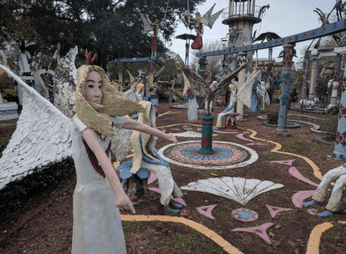 A whimsical outdoor sculpture garden featuring colorful angelic figures and intricate designs on the ground.