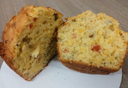 A loaf of cornbread, partially sliced, showing a moist texture with bits of vegetables and herbs throughout.