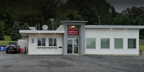Exterior view of the Pantry Restaurant, featuring a white building with a red sign and a gravel parking area.