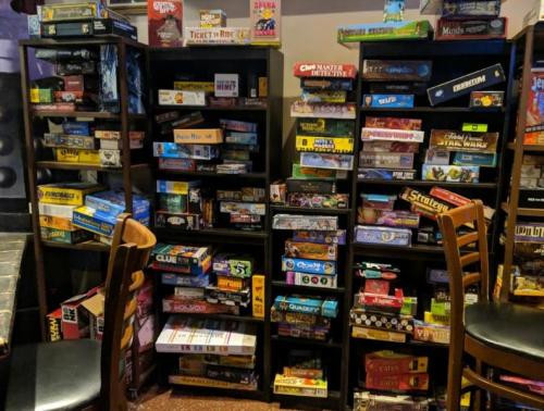 A cozy game room filled with shelves of various board games and a couple of empty chairs in the foreground.