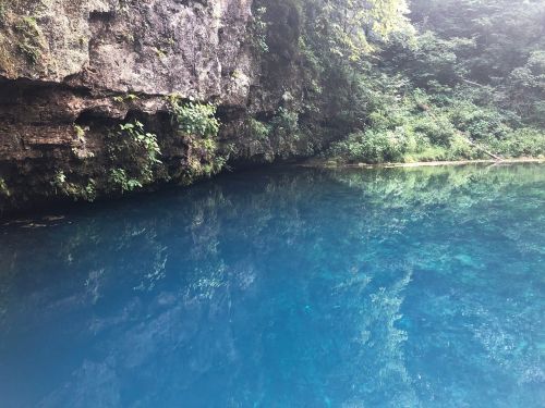 A serene blue body of water reflecting lush greenery and rocky cliffs in a tranquil natural setting.