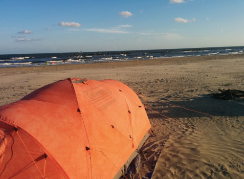 An orange tent on a sandy beach with gentle waves and a clear blue sky in the background.