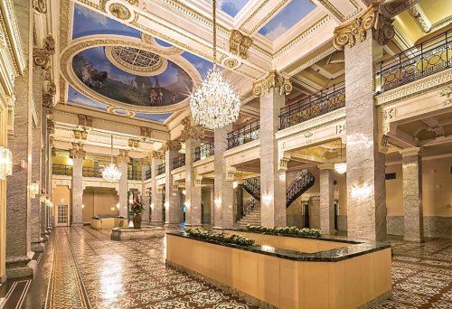 Elegant hotel lobby featuring marble columns, ornate chandeliers, and a beautifully painted ceiling.