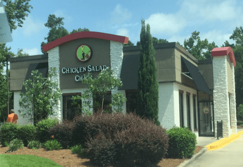 A restaurant building with a sign that reads "Chicken Salad Chick," surrounded by greenery and a clear blue sky.