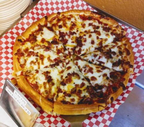 A freshly baked pizza with melted cheese and toppings, sliced and served on a red-checkered paper.