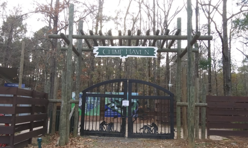 Entrance gate to Chimp Haven, surrounded by trees, featuring a wooden arch and a black gate with chimp silhouettes.