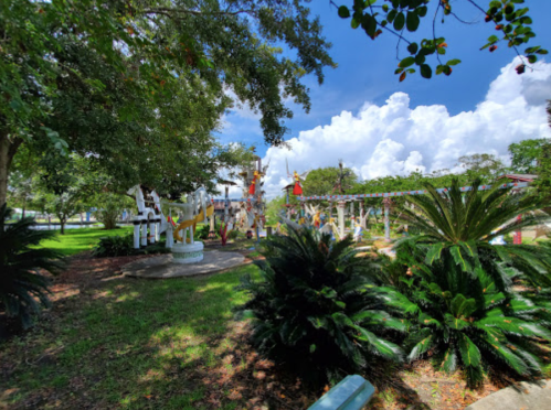 A vibrant park scene with colorful sculptures, lush greenery, and a bright blue sky with fluffy clouds.
