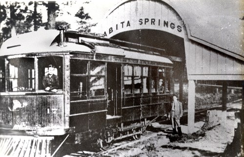 Historic black-and-white photo of a streetcar at the Abita Springs station, with a conductor and a man standing nearby.