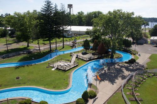 Aerial view of a winding water slide surrounded by green grass and trees, with a water tower in the background.