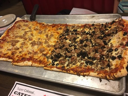 A large rectangular pizza divided into two sections: one with sausage and the other topped with olives and mushrooms.