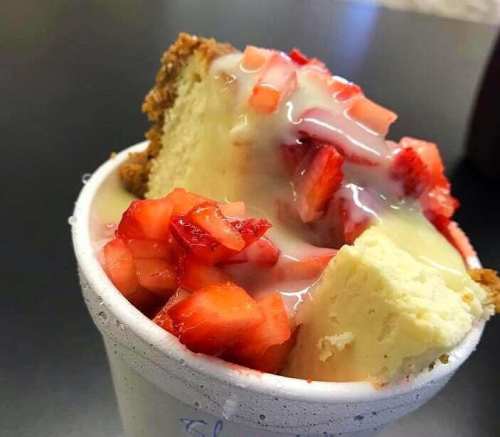 A cup filled with cake pieces topped with fresh strawberries and a creamy sauce.