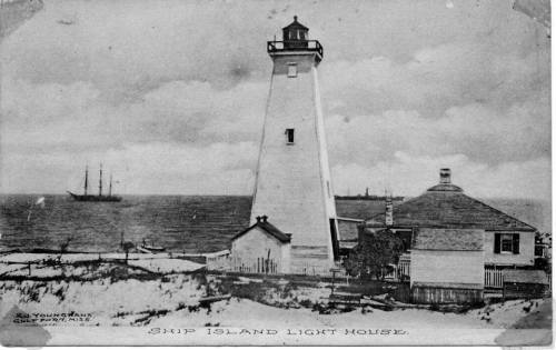 Black and white image of Ship Island Lighthouse with a ship in the background and a nearby house by the shore.