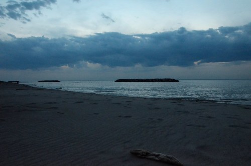 A serene beach at dusk, with gentle waves and a cloudy sky reflecting on the water.