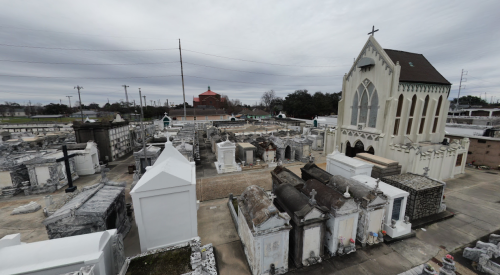 A panoramic view of a cemetery featuring mausoleums, gravestones, and a church under a cloudy sky.