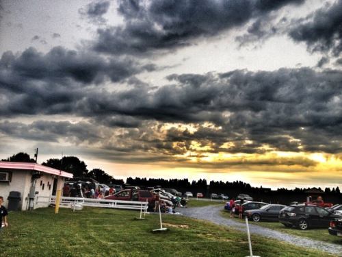 A parking area filled with cars under a dramatic sky, with dark clouds and a hint of sunset in the background.