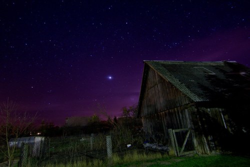 A rustic barn under a starry night sky with purple hues and a bright planet visible.
