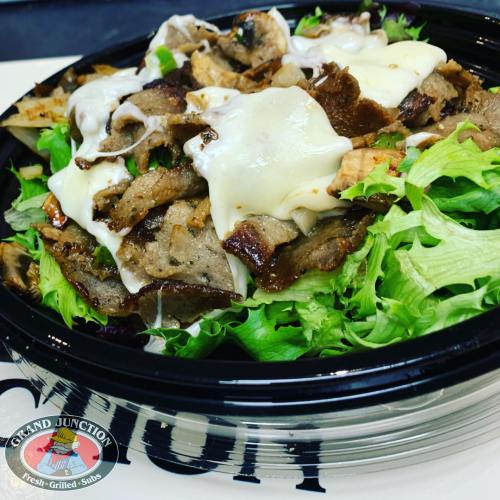 A bowl of salad topped with grilled meat, melted cheese, and fresh greens, served in a black container.