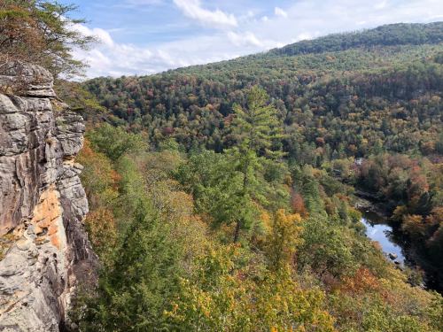 A scenic view of a forested valley with colorful autumn foliage and a river, framed by rocky cliffs under a blue sky.