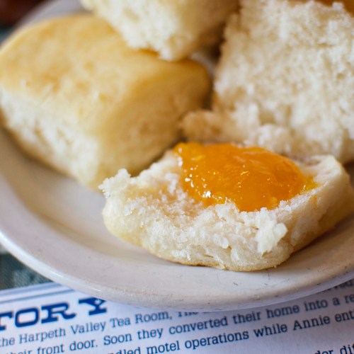 A close-up of a fluffy biscuit topped with a dollop of orange marmalade on a plate.