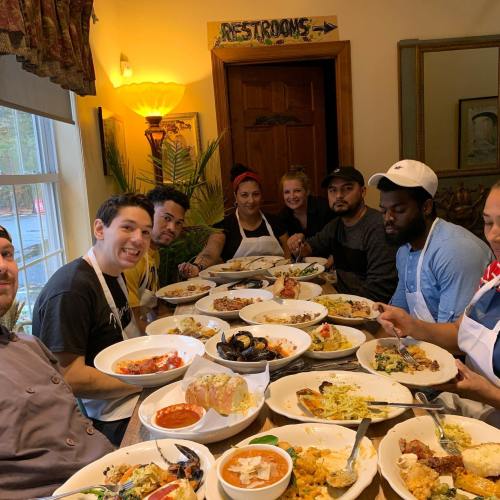 A group of people sitting around a table filled with various dishes, enjoying a meal together in a cozy setting.