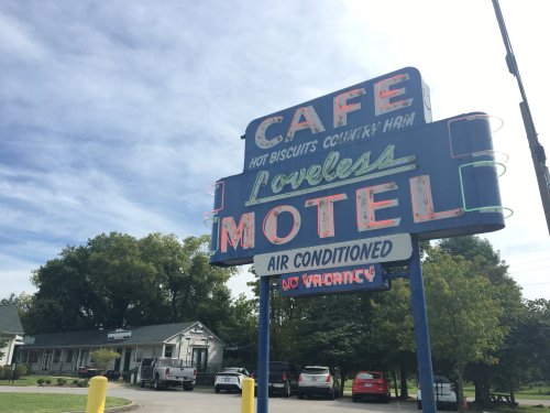 Sign for Loveless Motel and Cafe, featuring neon lights and a "No Vacancy" notice, set against a blue sky.