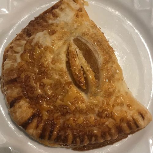 A golden-brown pastry with a shiny, sugary crust and a visible almond filling, served on a white plate.