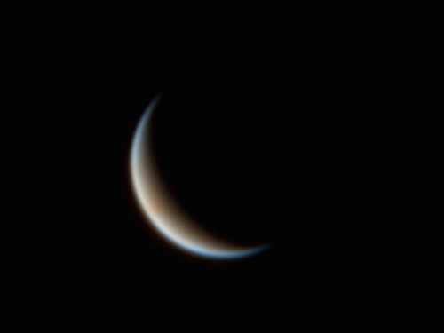 A close-up view of a crescent moon against a dark background, showcasing its smooth curve and subtle color gradient.